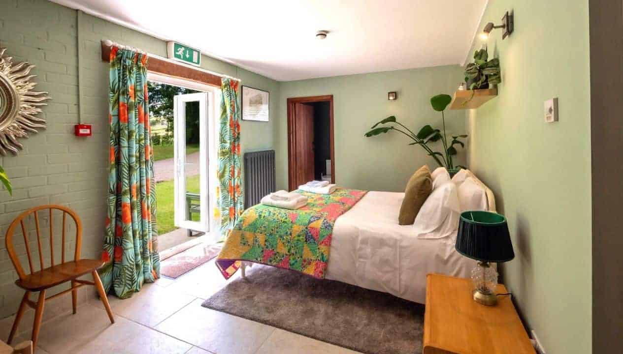 Monnow Valley Studio, Monmouthshire – Bedroom with colourful patterned bedspread, glass doors to garden, and potted plants.