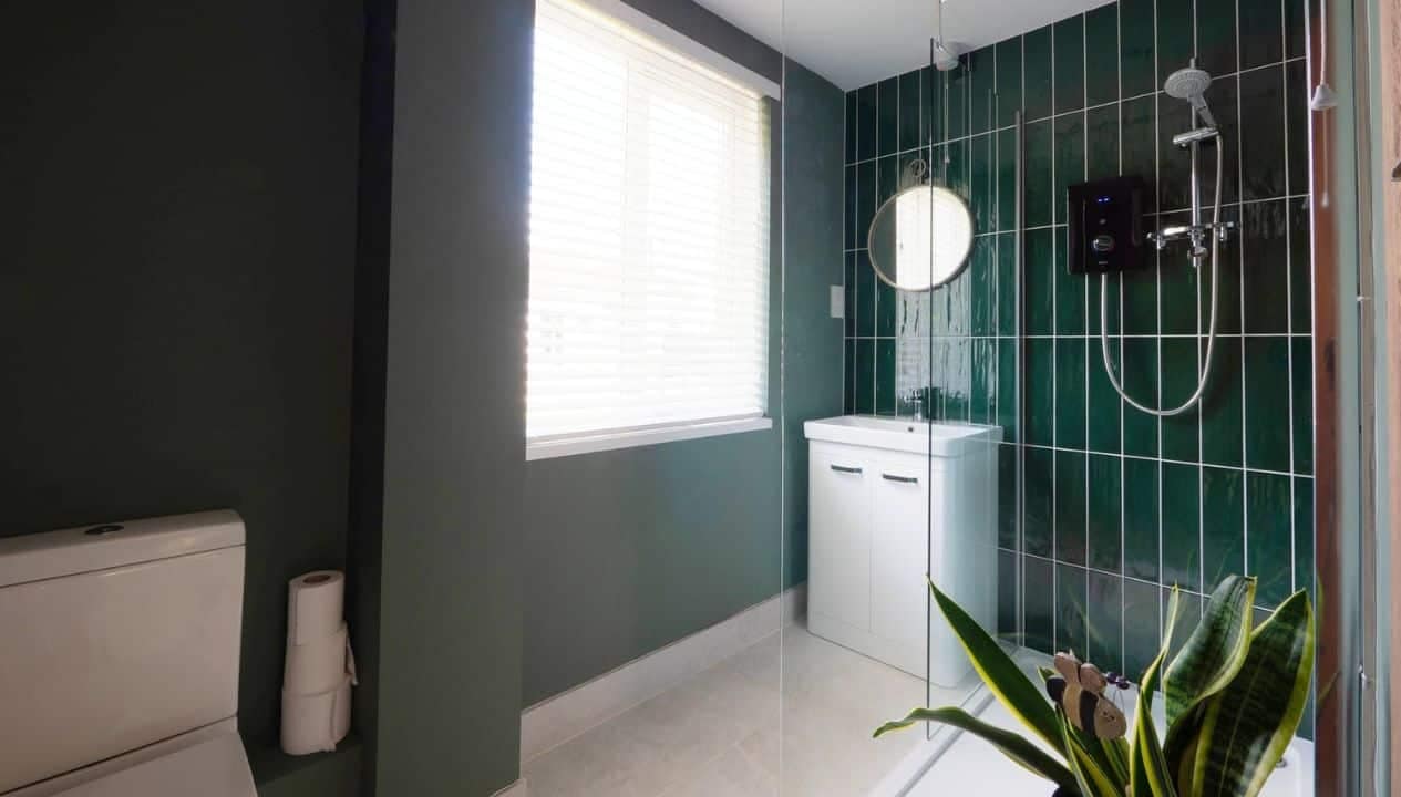 Monnow Valley Studio, Monmouthshire – Modern bathroom with dark green tiled walls, white vanity unit and walk-in shower.
