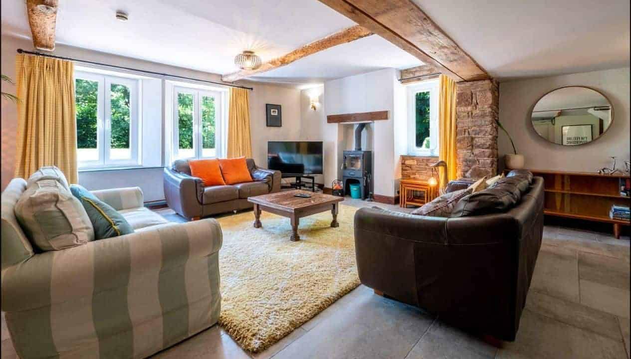 Monnow Valley Studio, Monmouthshire – Spacious open-plan living room with exposed timber beams, leather sofas and wood-burning stove.