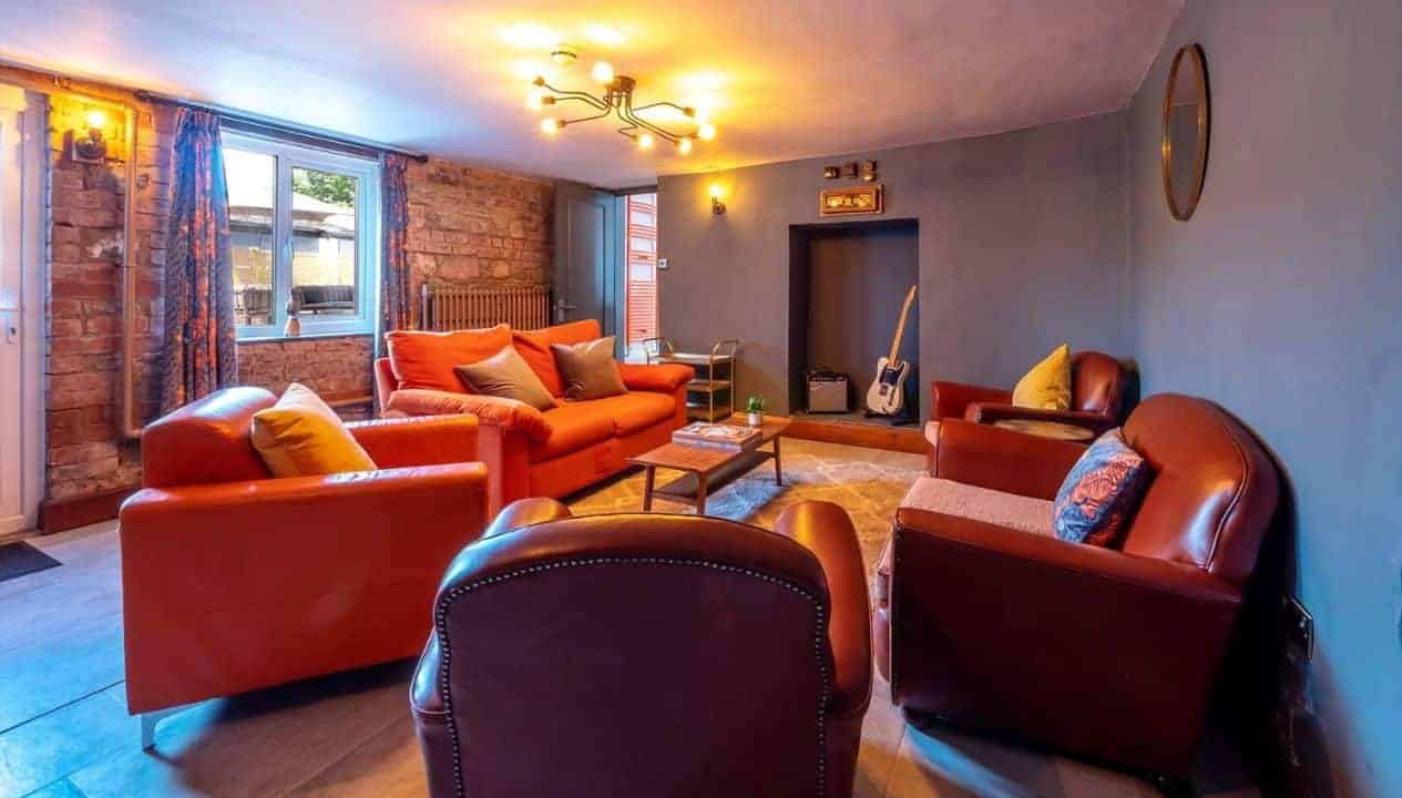 Monnow Valley Studio, Monmouthshire – Spacious lounge with red leather sofas, exposed brick walls, and electric ceiling lights.