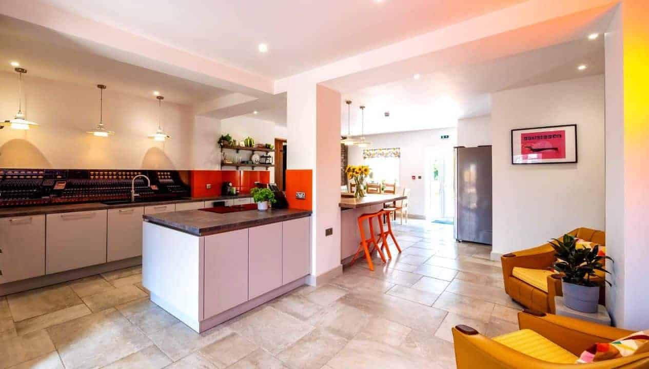 Monnow Valley Studio, Monmouthshire – Open-plan kitchen and living space with pink cabinetry, central island, and orange accents.