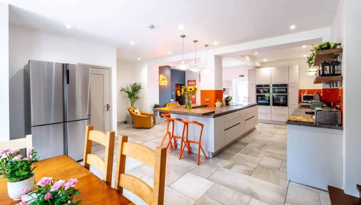 Monnow Valley Studio, Monmouthshire – Modern open-plan kitchen with central island, orange bar stools, and stainless steel appliances.