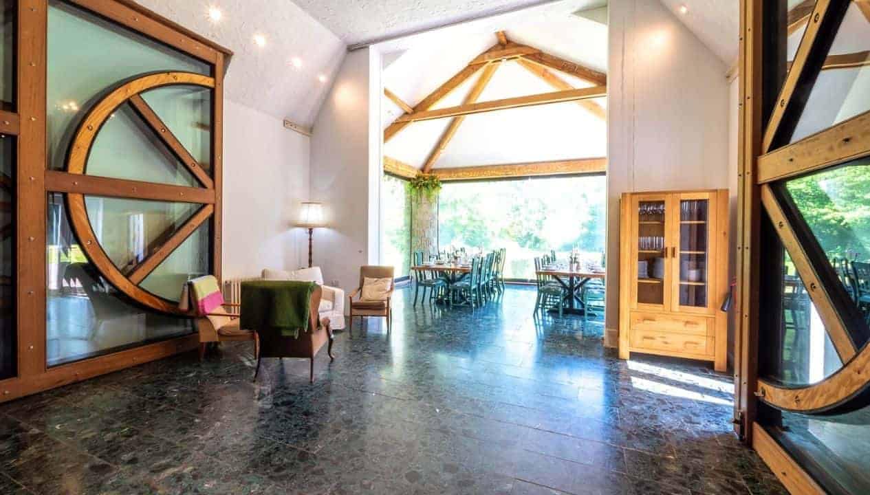 Monnow Valley Studio, Monmouthshire – Spacious open-plan interior with exposed wooden beams, large circular window and polished concrete flooring.