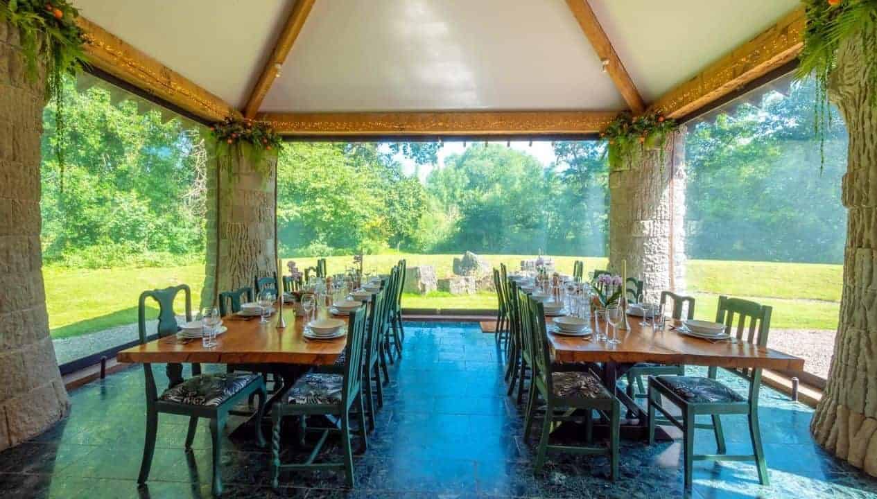 Monnow Valley Studio, Monmouthshire – Glazed dining pavilion with wooden beams, black chairs, and views across grounds.