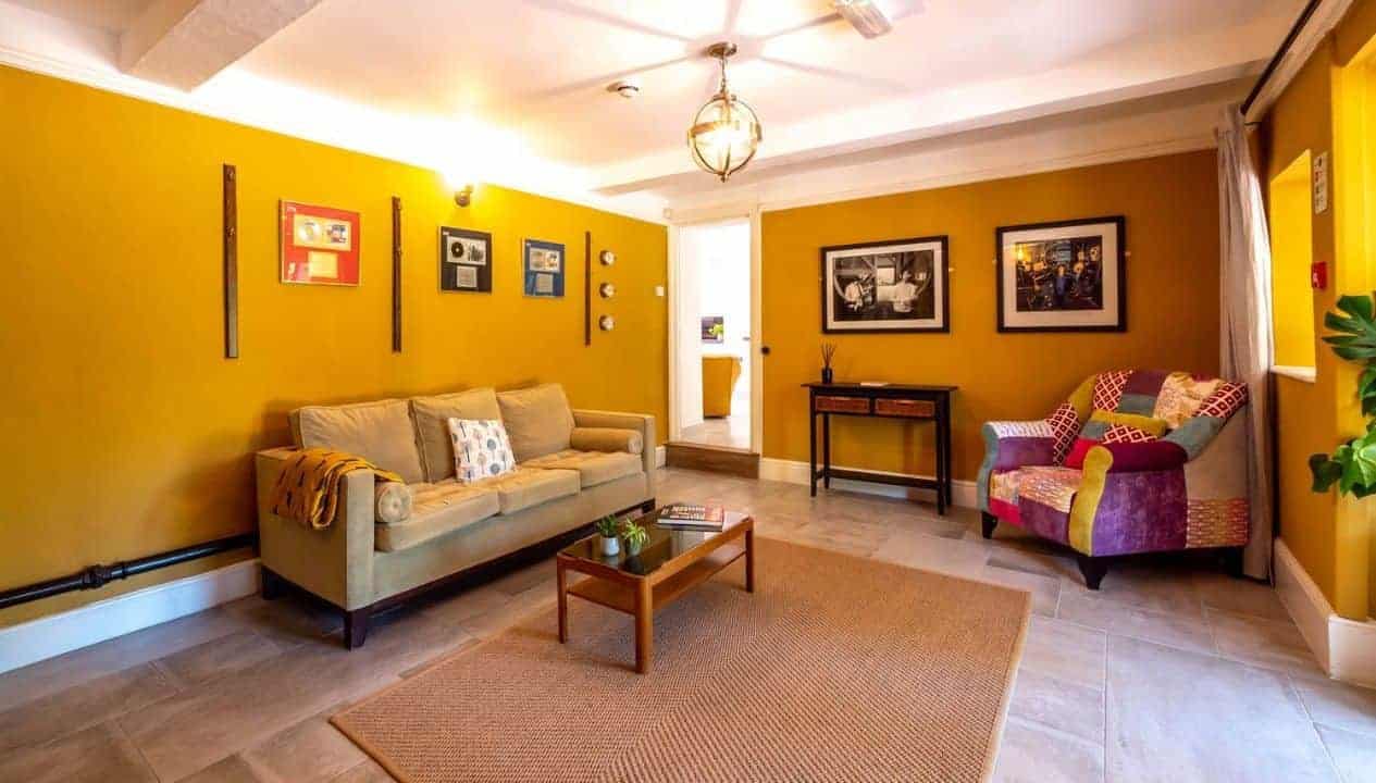 Monnow Valley Studio, Monmouthshire – Bright yellow living room with beige sofa, patterned armchair, and wooden coffee table.