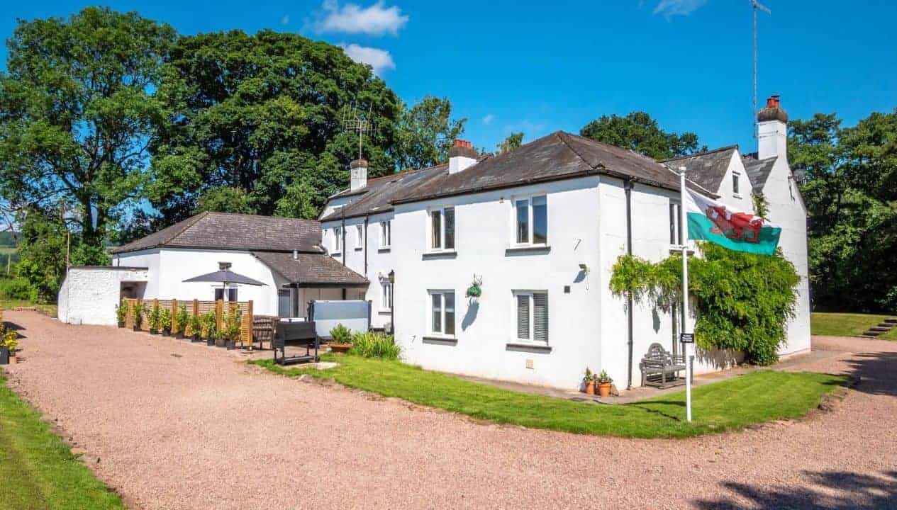 Monnow Valley Studio, Monmouthshire – White-rendered country house with gravel courtyard and Welsh flag, surrounded by mature trees.