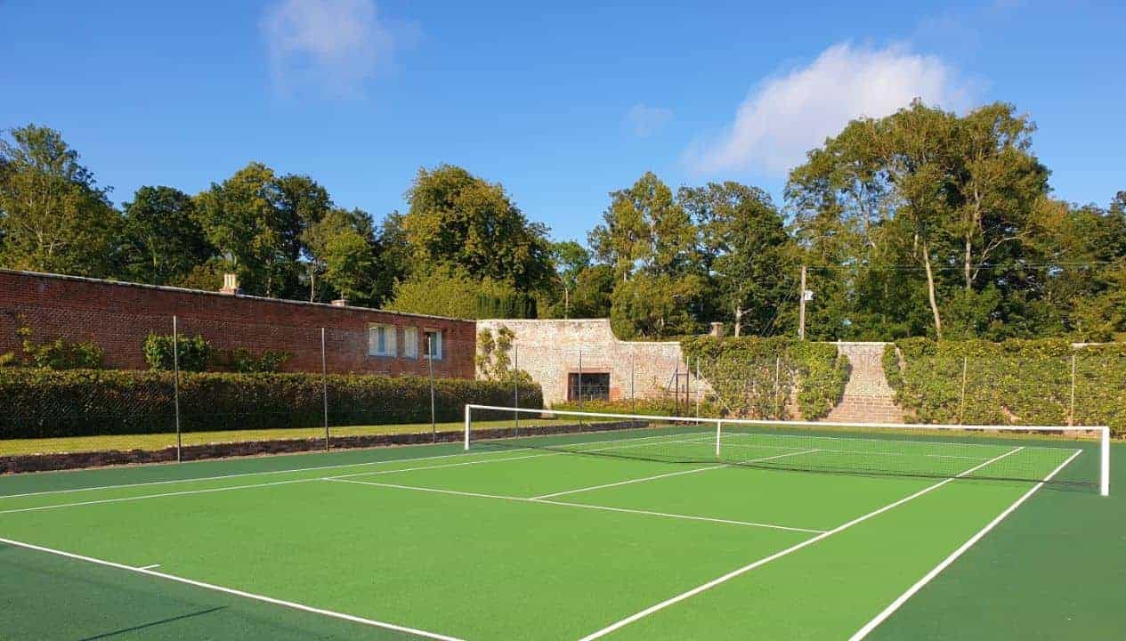 Leuchie Walled Garden – Tennis court with green playing surface and brick outbuildings surrounded by mature trees.