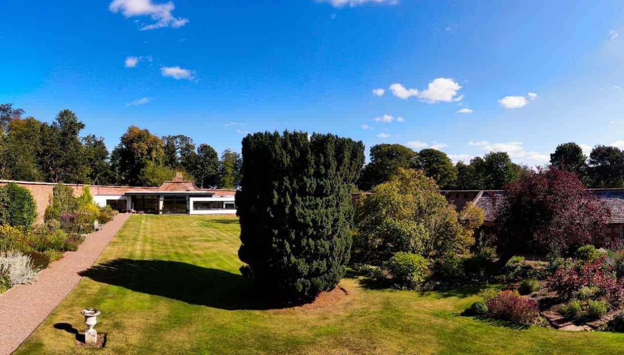 Leuchie Walled Garden – Modern single-storey brick building with manicured lawns and mature specimen trees including tall conifers.