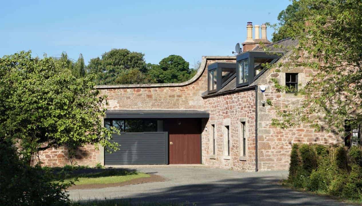 Leuchie Walled Garden – Stone cottage with modern extension, black-framed garage and red door, mature hedging.