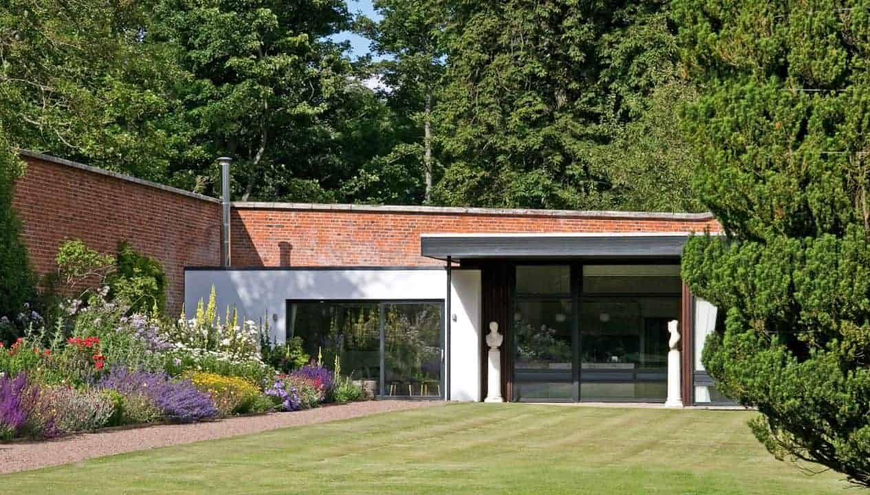 Leuchie Walled Garden – Modern brick extension with large glazed doors, herbaceous borders, and mature woodland backdrop.