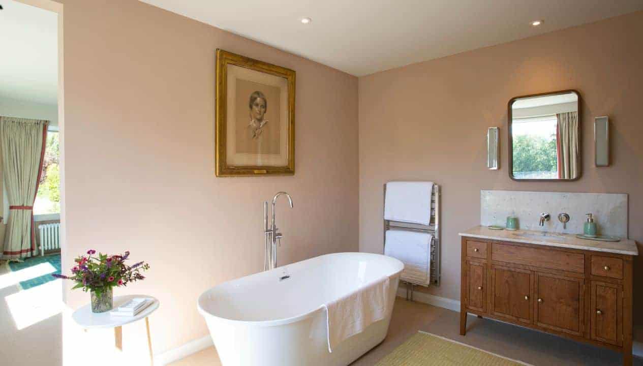 Leuchie Walled Garden – Spacious bathroom with freestanding white bathtub, wooden vanity unit and portrait artwork.