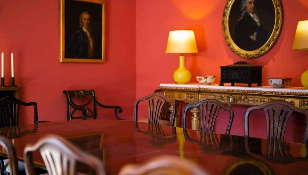 Leuchie Walled Garden – Formal dining room with coral-red walls, mahogany table, and gilt-framed portraits.