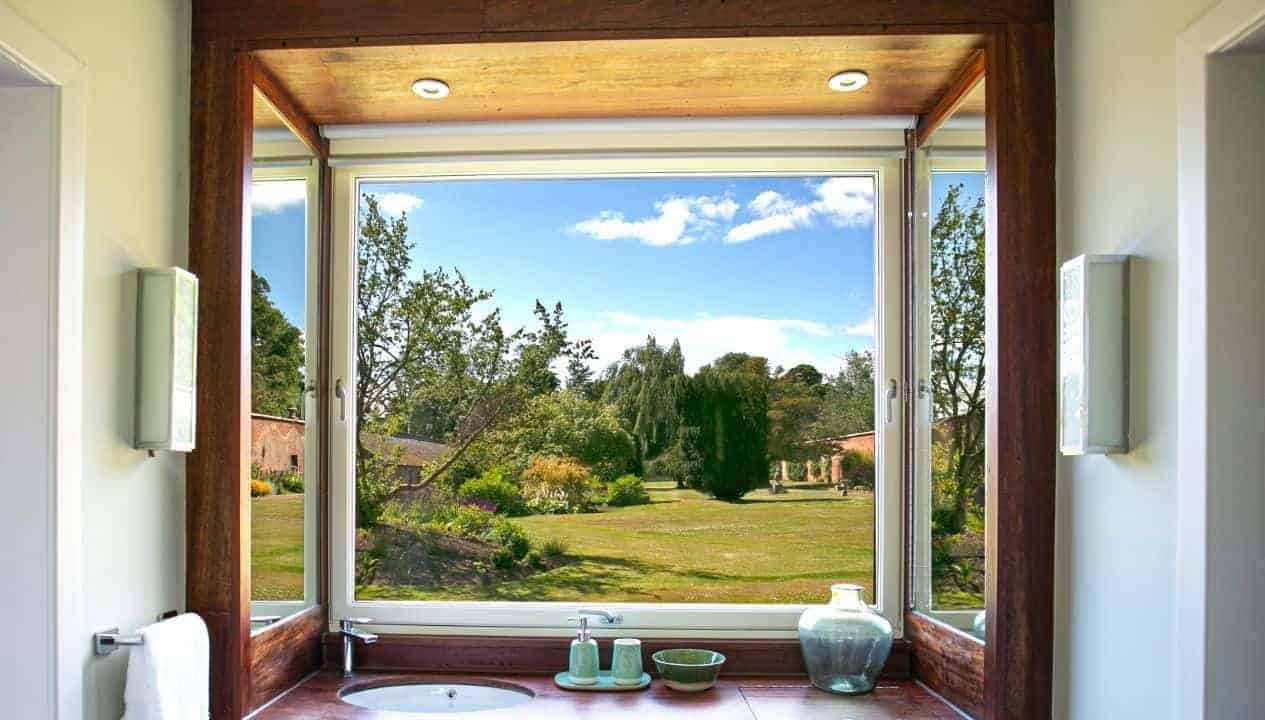 Leuchie Walled Garden – Bathroom with wooden-framed window overlooking manicured grounds and stone outbuildings.