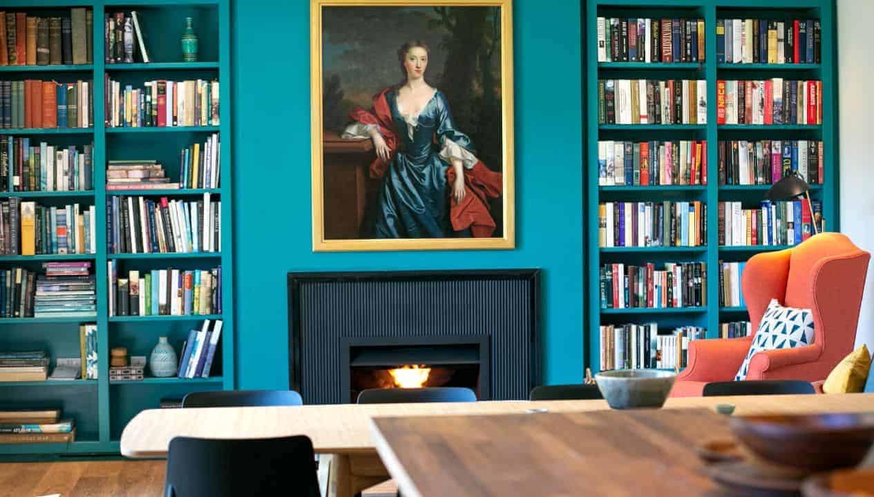 Leuchie Walled Garden – Library with turquoise built-in bookshelves, black fireplace, and portrait painting.