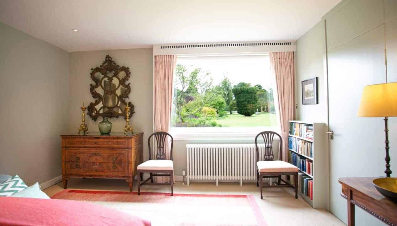 Leuchie Walled Garden – Bedroom with antique chest of drawers, window overlooking garden grounds, two upholstered chairs.