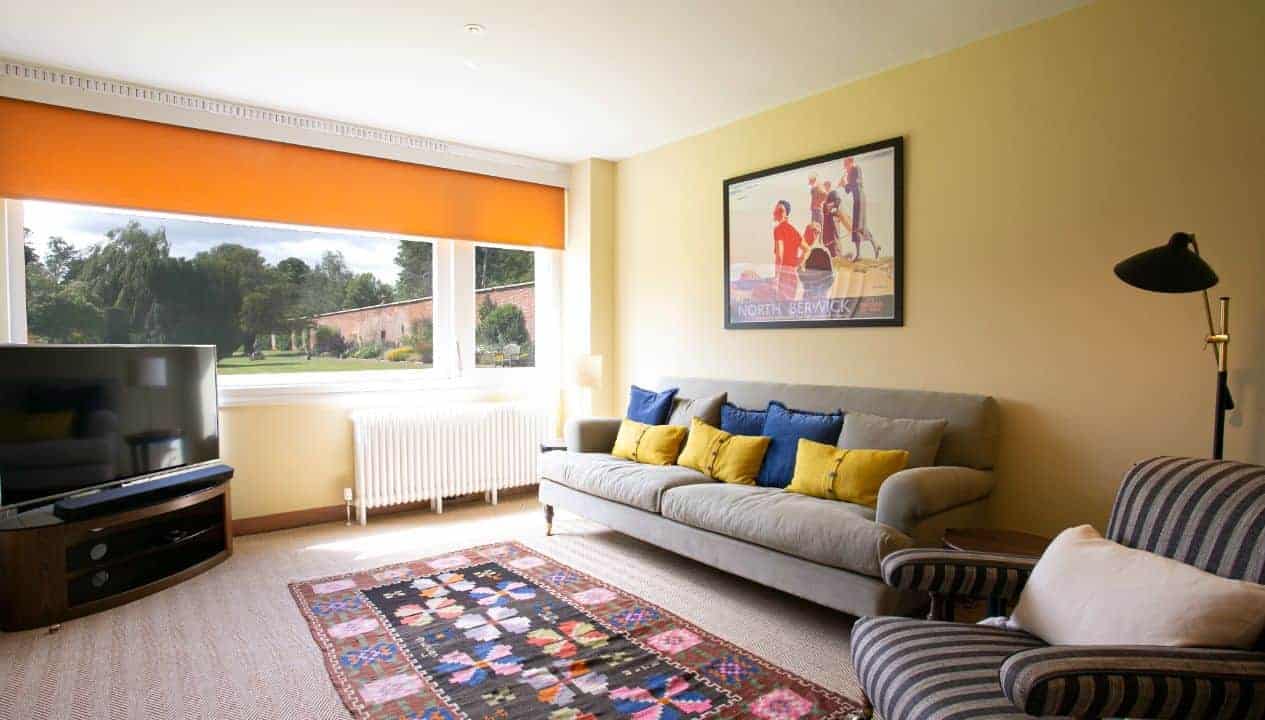 Leuchie Walled Garden – Spacious living room with grey sofa, yellow and blue cushions, patterned rug, and garden views.