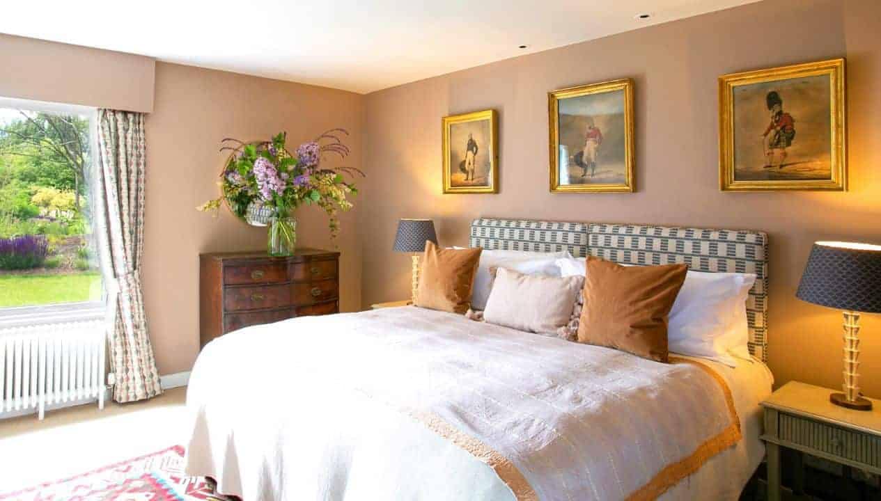 Leuchie Walled Garden – Bedroom with patterned headboard, gold-framed portraits, and garden views through sash window.