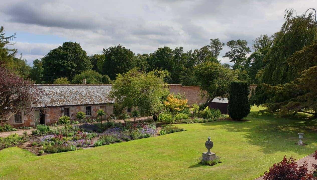 Leuchie Walled Garden – Brick cottage with slate roof, manicured lawn, herbaceous borders and stone urn ornament.