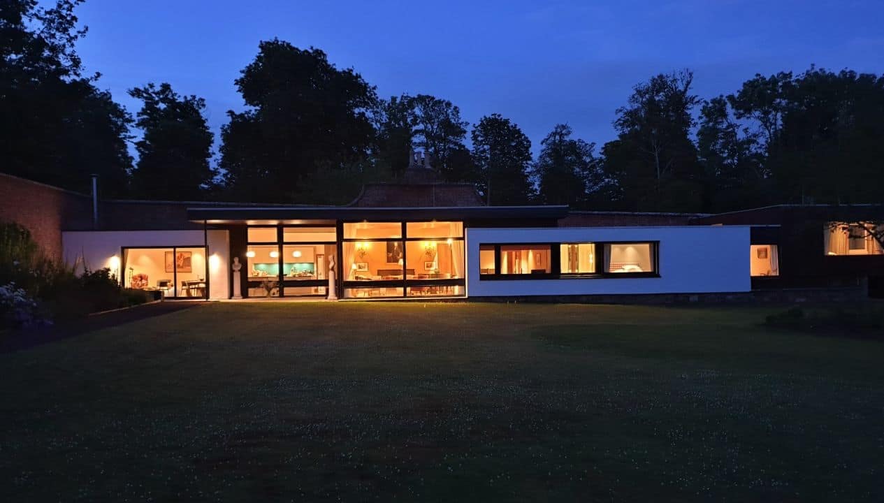 Leuchie Walled Garden – Modern single-storey house illuminated at dusk with large glazed windows and woodland backdrop.