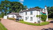 Monnow Valley Studio, Monmouthshire – White-rendered country house with gravel courtyard and Welsh flag, surrounded by mature trees.