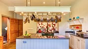 Gitcombe House, Devon – Kitchen with suspended copper pan rack and colourful tiled splashback above Aga cooker.