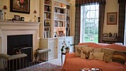 The Old House, Hampshire – Cream sitting room with fireplace, built-in bookshelves, and orange upholstered sofa.