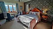 Bossington Hall, Somerset – Master bedroom with four-poster bed, damask wallpaper and bay windows overlooking countryside.
