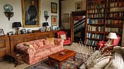 Boxted Hall, Suffolk – Library lounge with red damask sofa, wooden bookshelves, and period portraits.