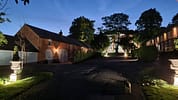 Breedon Hall, Leicestershire – Illuminated brick courtyard with converted barn buildings and mature trees at dusk.