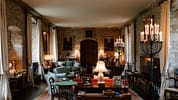 Ferniehirst Castle, East Lothian – Grand stone hall with arched doorway, candelabra lighting, and upholstered seating.