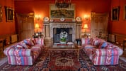 Gilmerton House, East Lothian – Formal drawing room with red walls, ornate fireplace, and striped sofas.