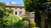 Gitcombe House, Devon – Brick country house with manicured lawn and formal entrance portico behind wooden gate.