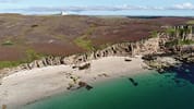 House of the Northern Gate, Highland – Coastal cliffs, sandy beach and turquoise water with distant white house on moorland.