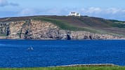 House of the Northern Gate, Highland – White mansion on rocky headland overlooking blue sea and coastal cliffs.