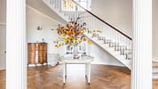 Manar House, Aberdeenshire – Entrance hall with curved staircase, autumn foliage arrangement and herringbone wooden flooring.