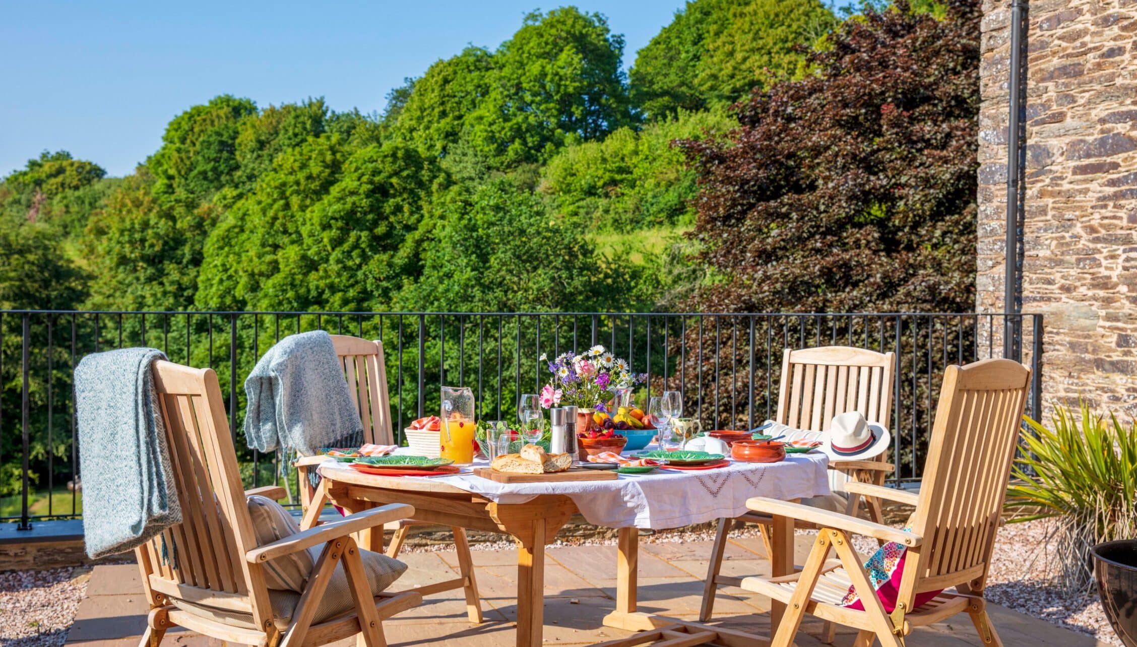 Gitcombe House, Devon – Terrace dining table with wooden chairs overlooking wooded countryside views.