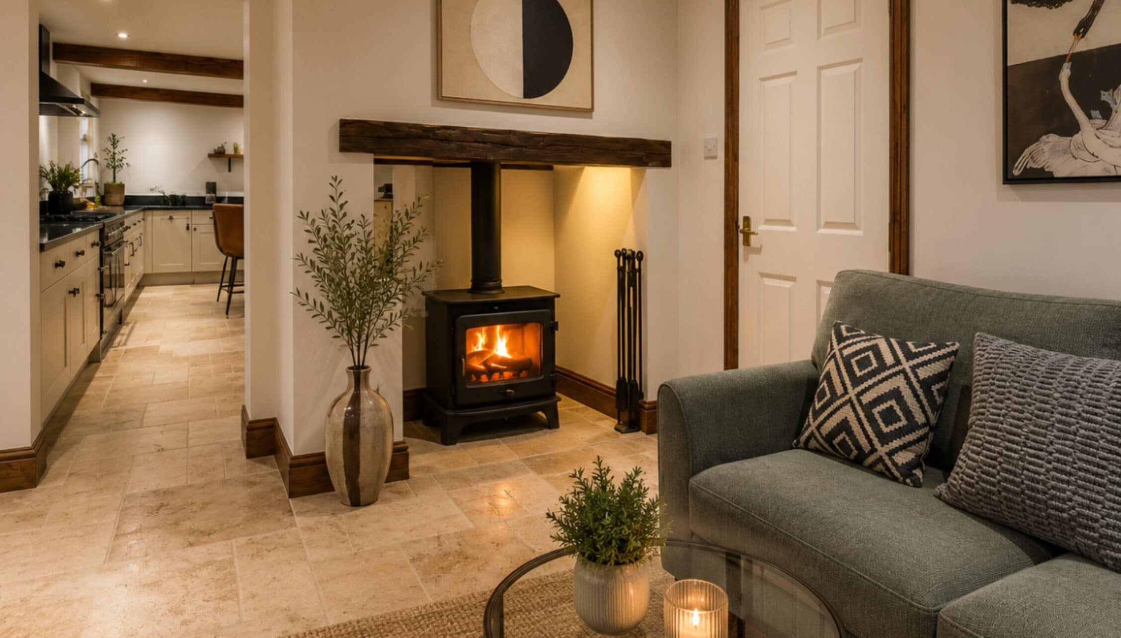 Catton Old Hall, Norfolk – Open-plan living space with wood-burning stove, grey sofa, and kitchen visible through archway.