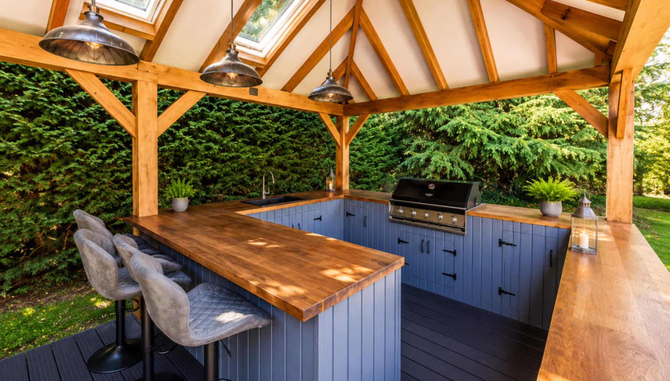 Catton Old Hall, Norfolk – Covered oak pavilion with blue cabinetry, built-in barbecue, and bar seating.