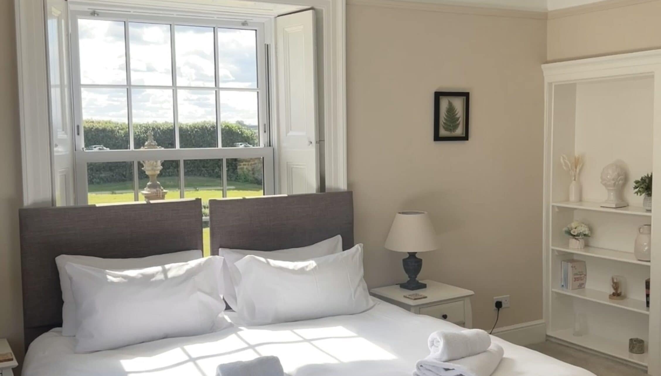 Greens Norton House, Northamptonshire — Bedroom with sash windows overlooking gardens, dark wood bed frame, white bedding.