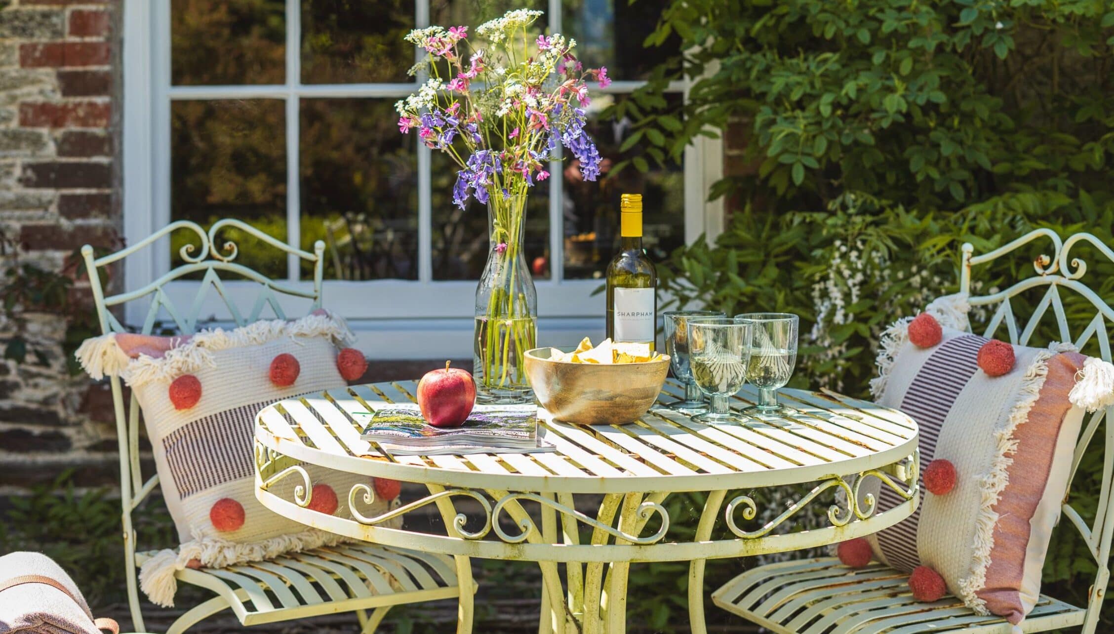 Gitcombe House, Devon – Cream metal garden table and chairs with floral arrangement and wine bottle on terrace.