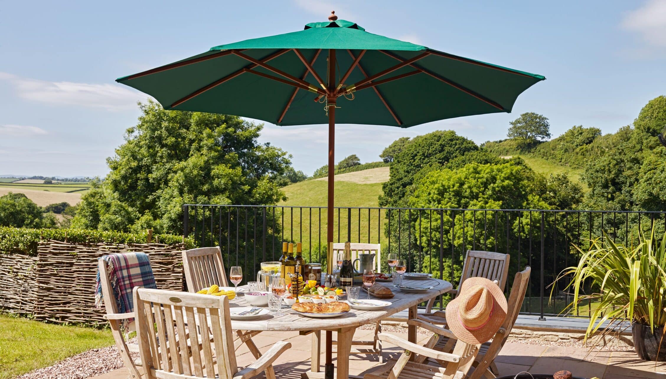 Gitcombe House, Devon – Terrace dining area with green parasol overlooking rolling countryside and hedgerow borders.
