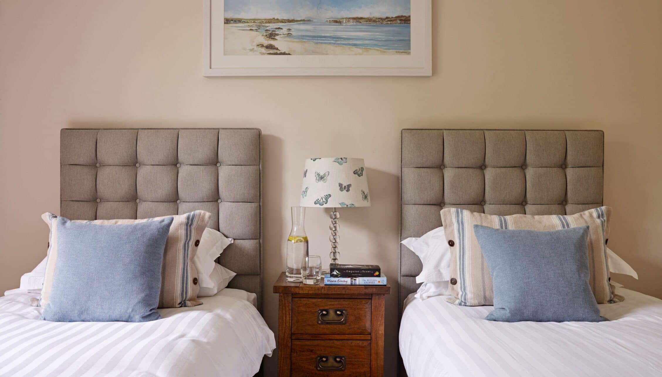 Gitcombe House, Devon – Twin single beds with upholstered headboards and blue cushions, wooden bedside table.