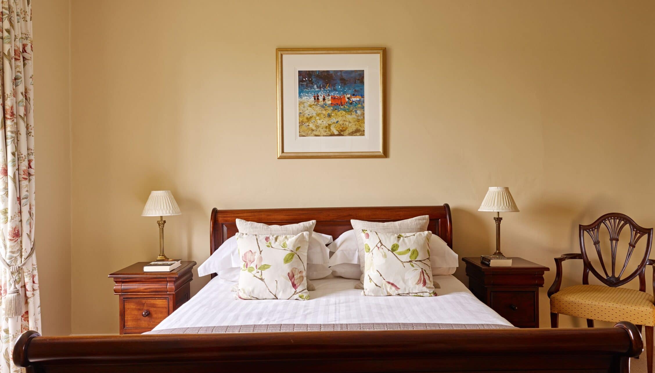 Gitcombe House, Devon – Bedroom with mahogany sleigh bed, cream walls, and framed beach scene artwork.