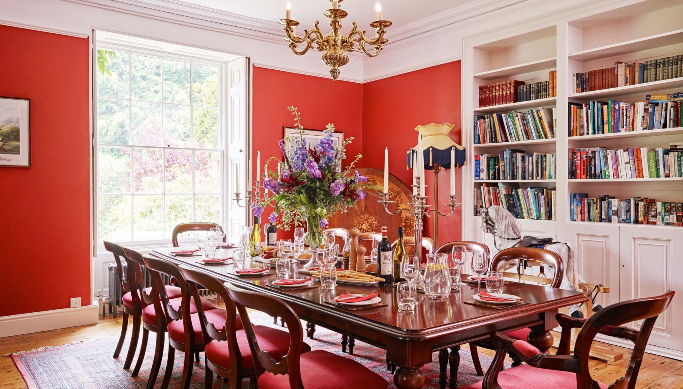 Gitcombe House, Devon – Formal dining room with red walls, mahogany table, and built-in bookshelves.