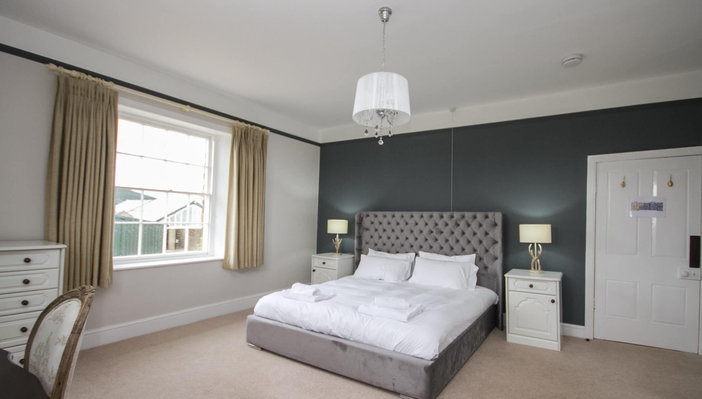Greens Norton House, Northamptonshire — Master bedroom with grey feature wall, upholstered bed and countryside views.
