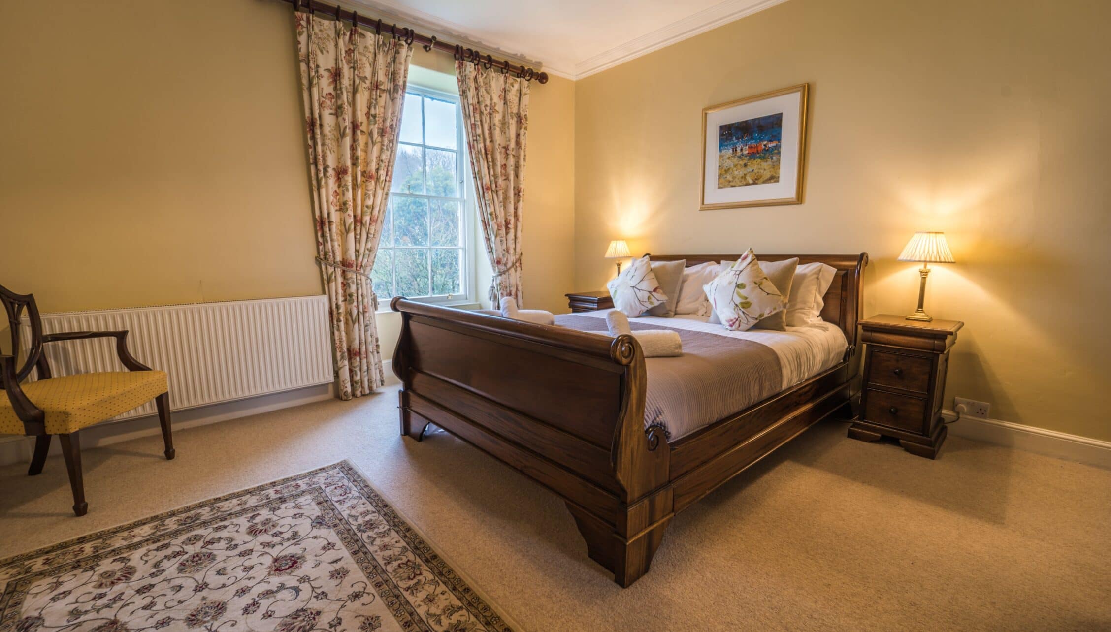 Gitcombe House, Devon – Master bedroom with wooden sleigh bed, patterned curtains, and countryside views.