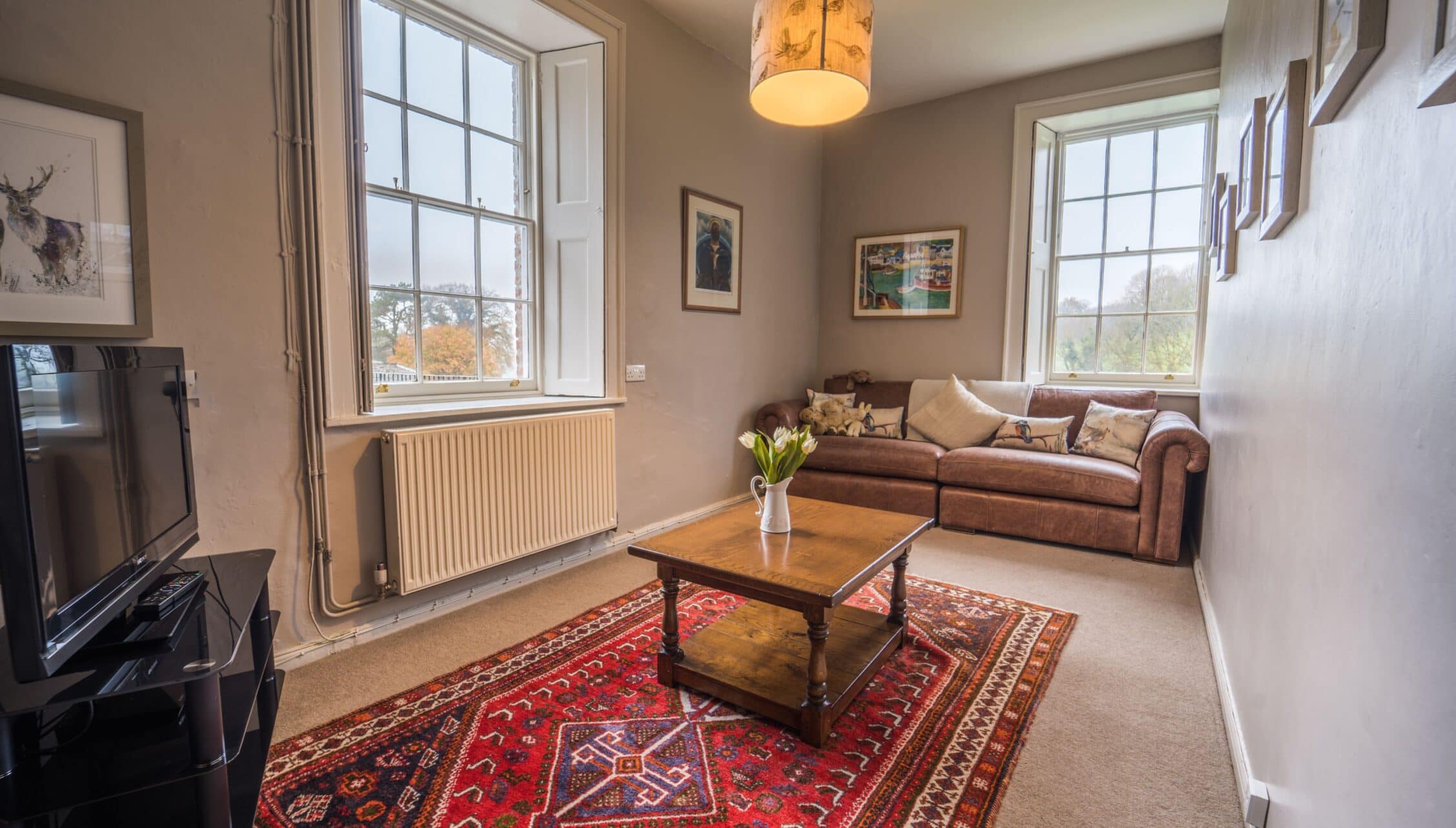 Gitcombe House, Devon – Spacious sitting room with sash windows, wood coffee table and burgundy Persian rug.