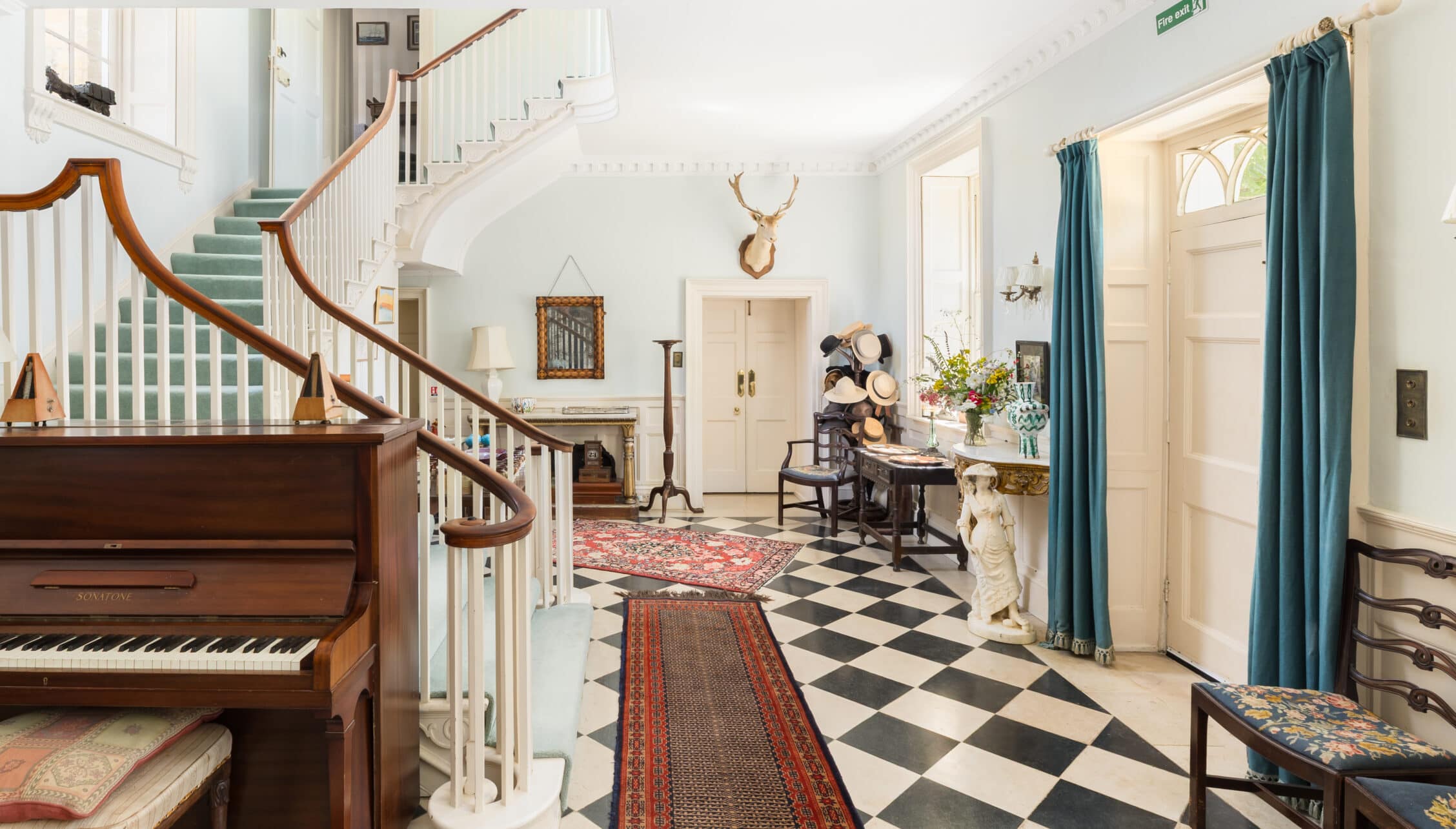 Upper Court, Gloucestershire – Grand entrance hall with curved wooden staircase, black and white tiled floor, and piano.