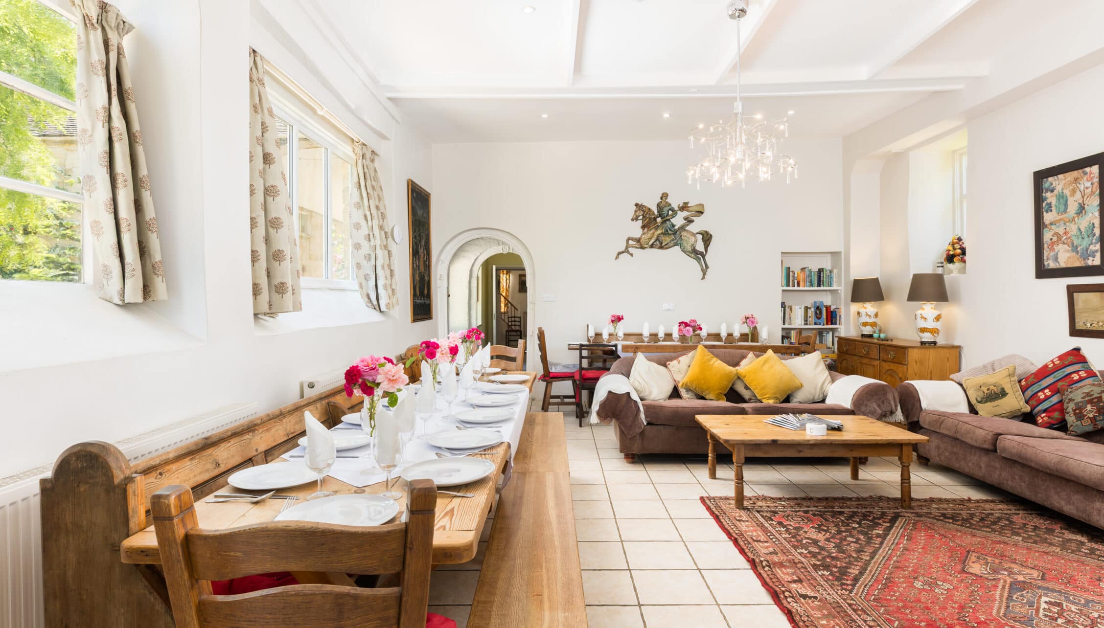 Upper Court, Gloucestershire – Open-plan dining and sitting room with wooden table, sofa, and crystal chandelier.