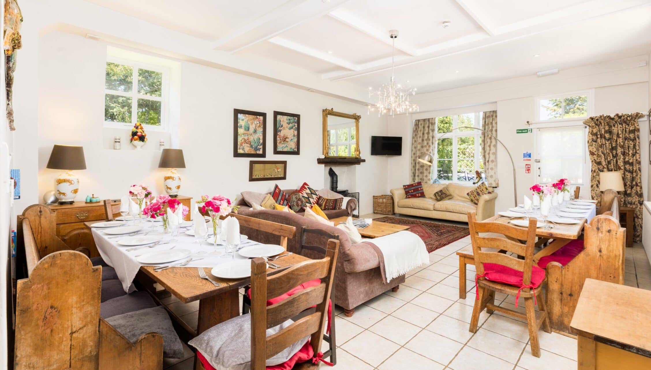 Upper Court, Gloucestershire – Open-plan living space with wooden dining table, upholstered seating, and bright floral arrangements.